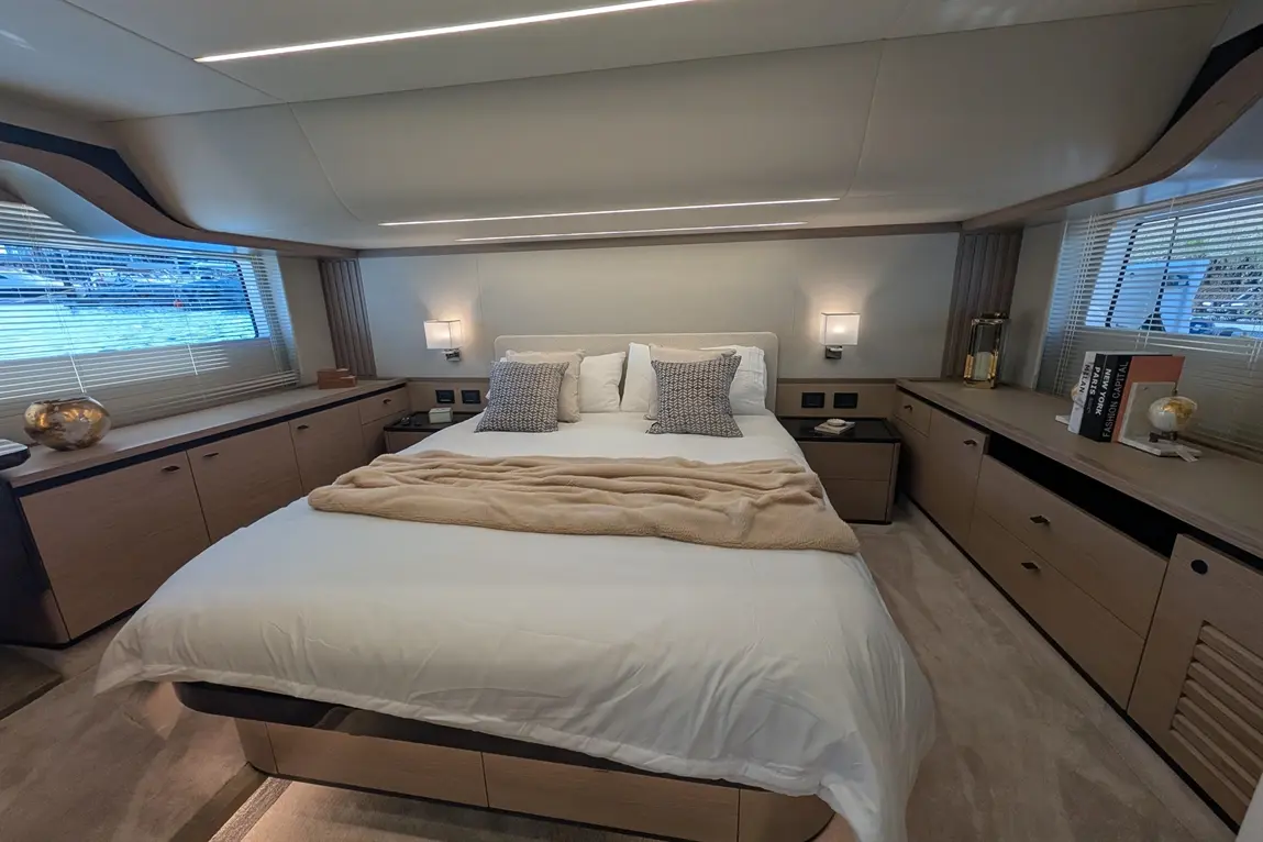 Luxury yacht bedroom featuring a king-size bed, soft bedding, decorative cushions, and stylish wooden furnishings.
